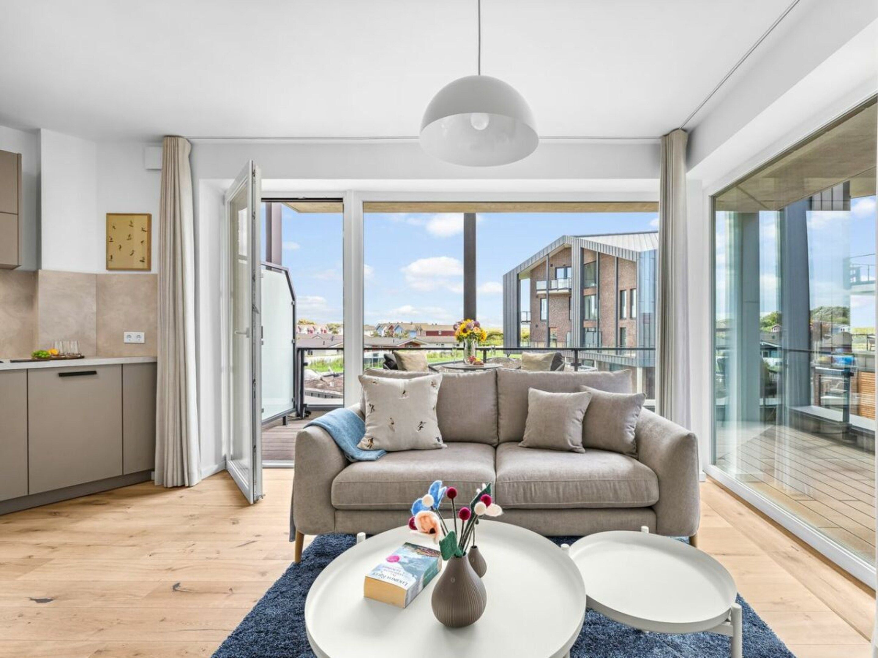 A modern living room with a sofa, coffee table, and a view of a cityscape through large windows.