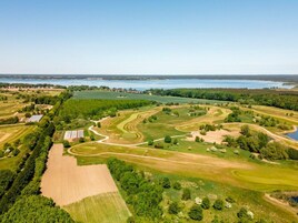 Vista aérea de un campo de golf con múltiples áreas verdes, calles de juego y una gran masa de agua al fondo.