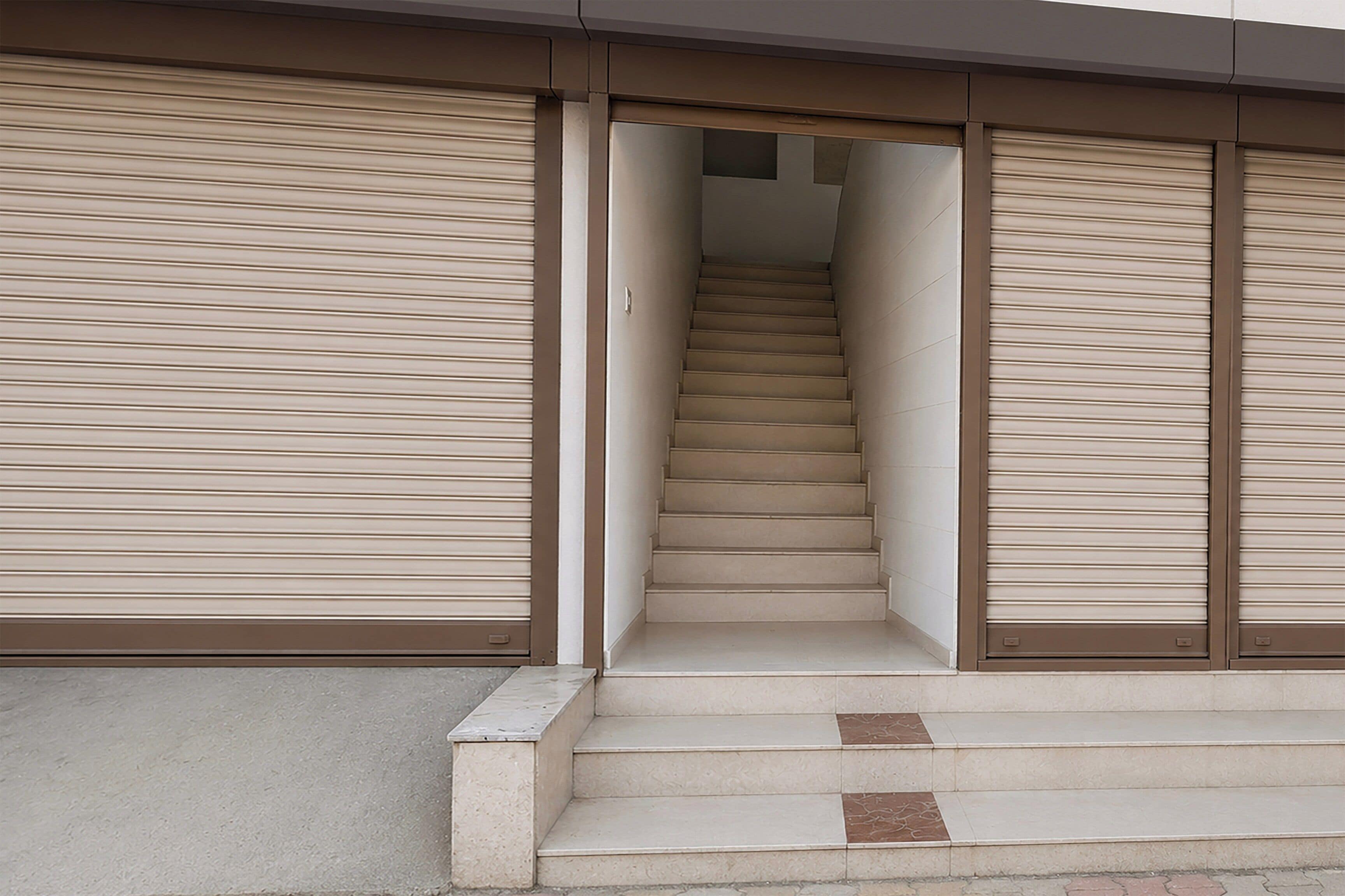 A staircase leading to an upper floor with closed roller shutters on either side.