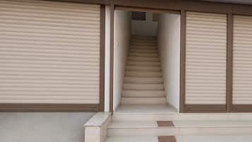 A staircase leading to an upper floor with closed roller shutters on either side.