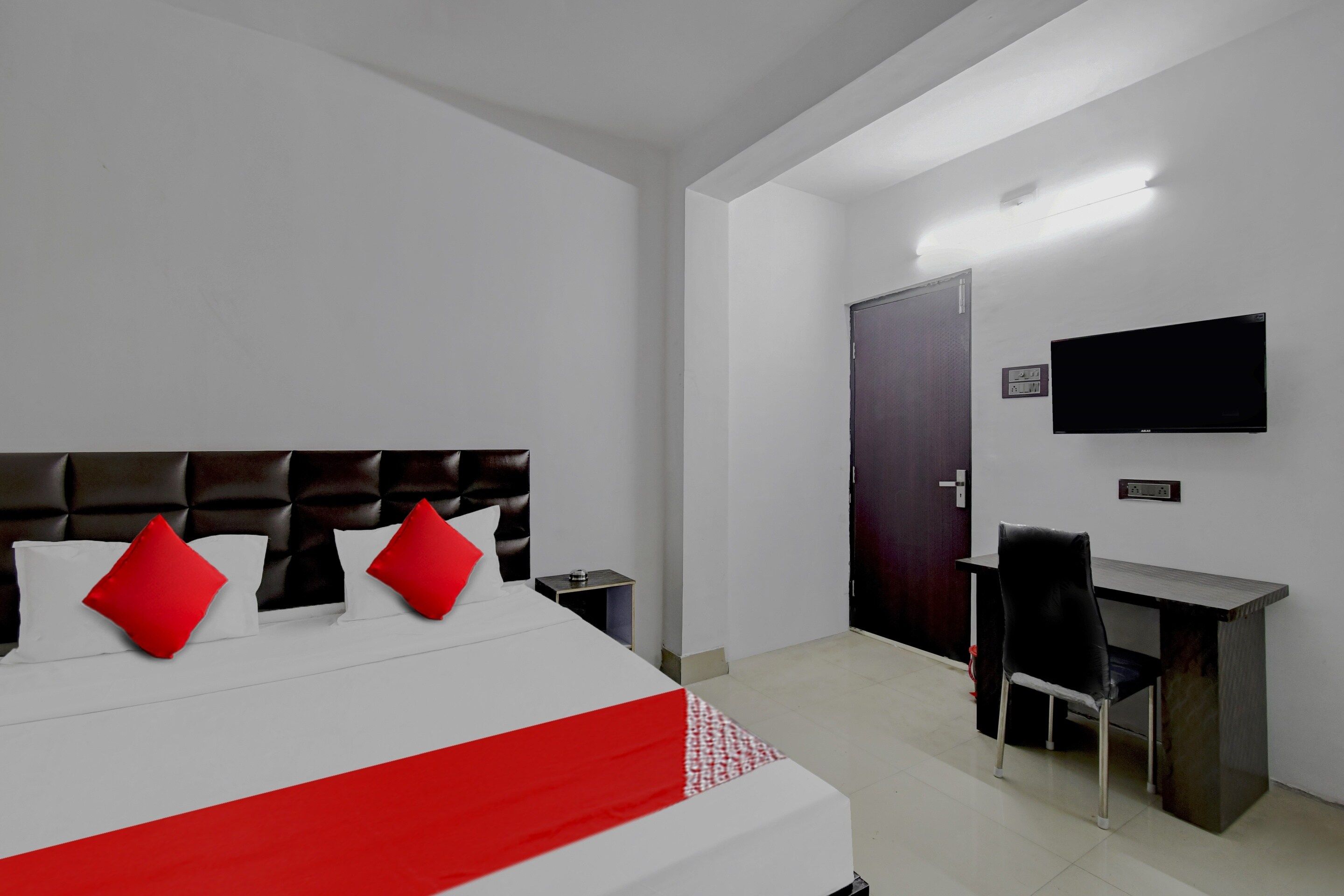 A hotel room with a bed, a desk, a chair, a TV, and a door.