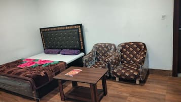 Quarto com cama, duas poltronas, uma mesinha de madeira e parede branca.