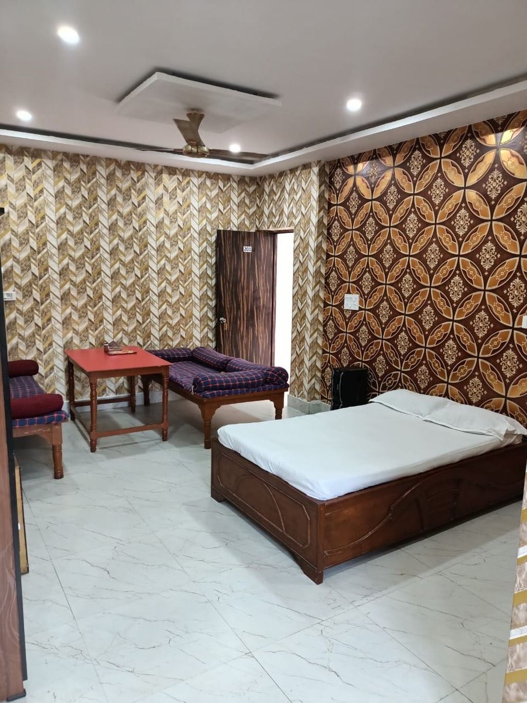 A bedroom with a bed, a table, two chairs, a ceiling fan, and patterned wallpaper.