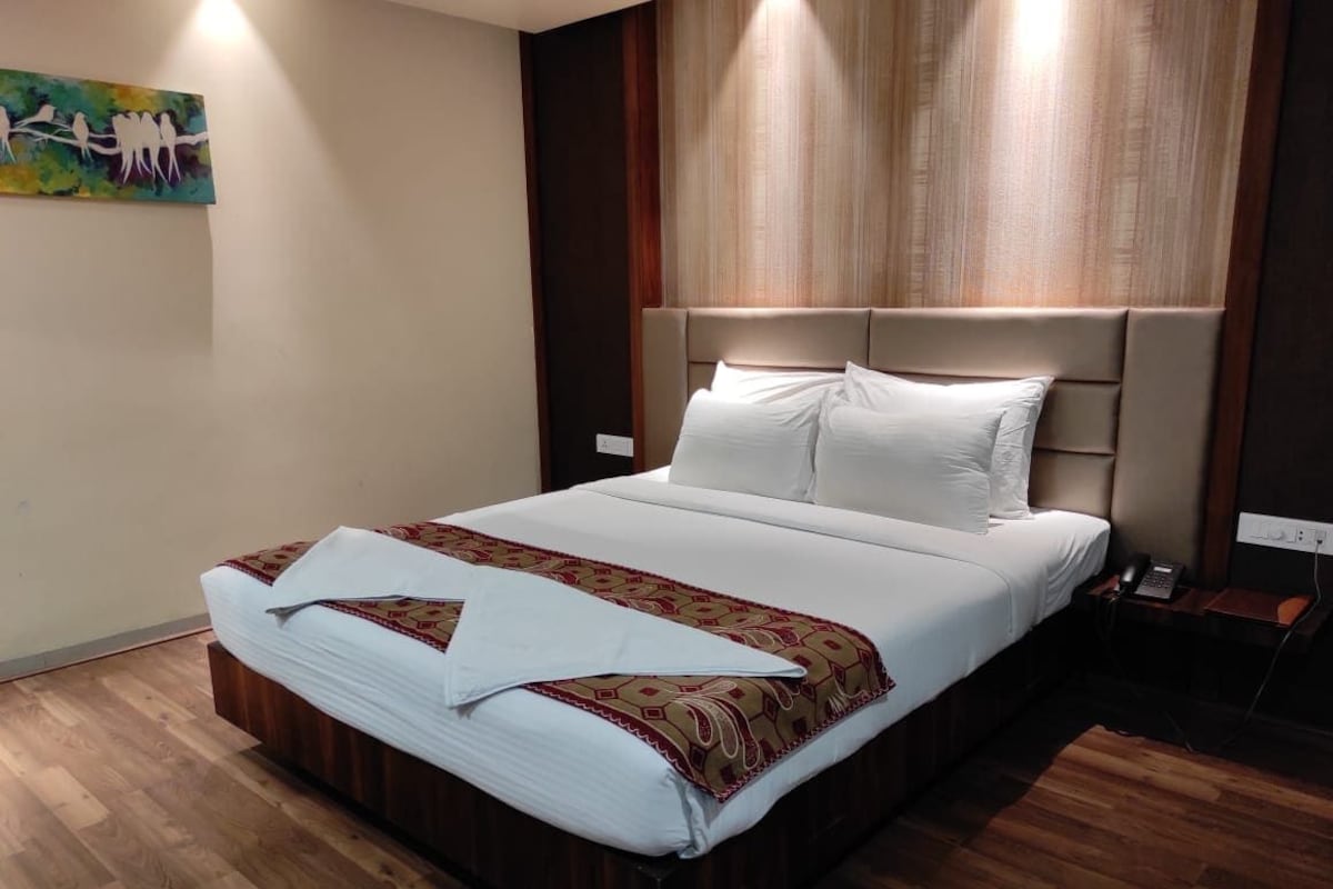Un letto rifatto con cura, una coperta a motivi decorativi e cuscini, un pavimento in legno, un quadro appeso al muro e un comodino con un telefono.