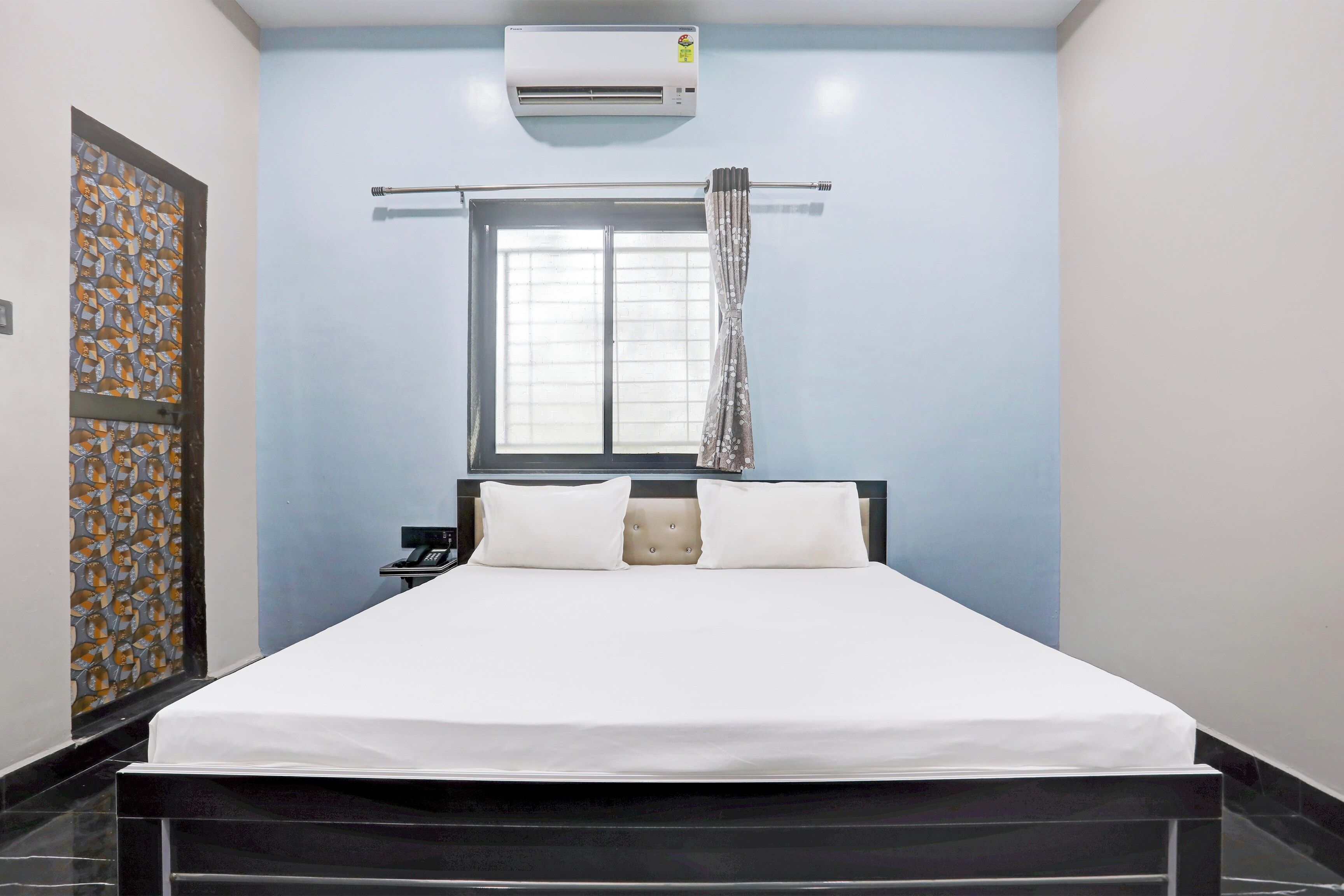 Une chambre d’hôtel équipée d’un lit, d’un téléphone, d’un appareil de climatisation et d’une fenêtre avec des rideaux.