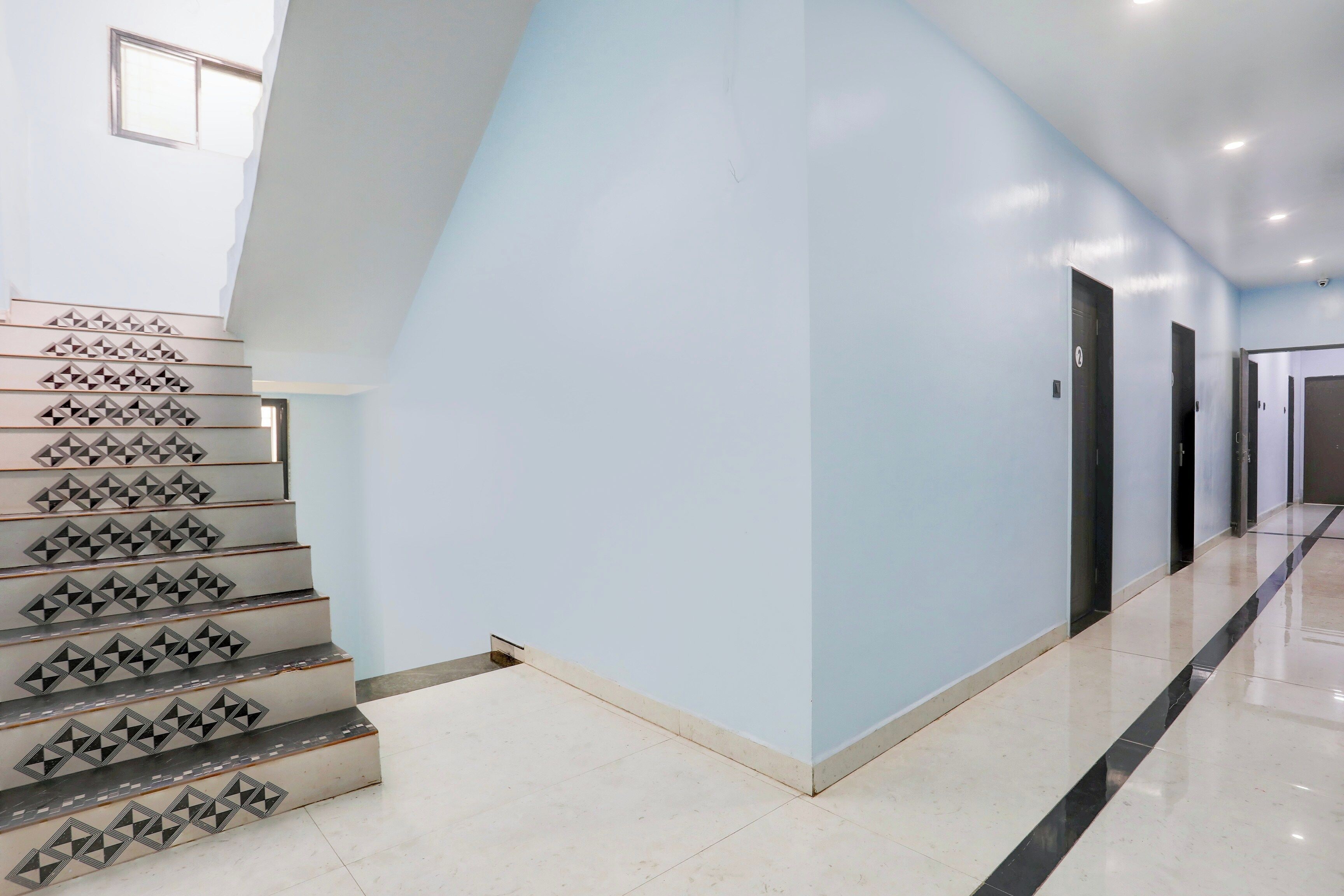 A modern interior with a staircase featuring geometric patterns, light blue walls, and a clean, polished floor.