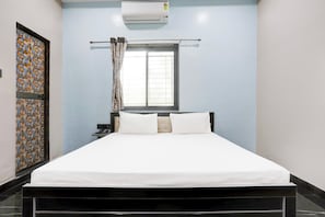Ein Hotelzimmer mit einem Bett, einem fensterbelaubten Fenster, einer Wandklimaanlage und einer gestalteten Tür.