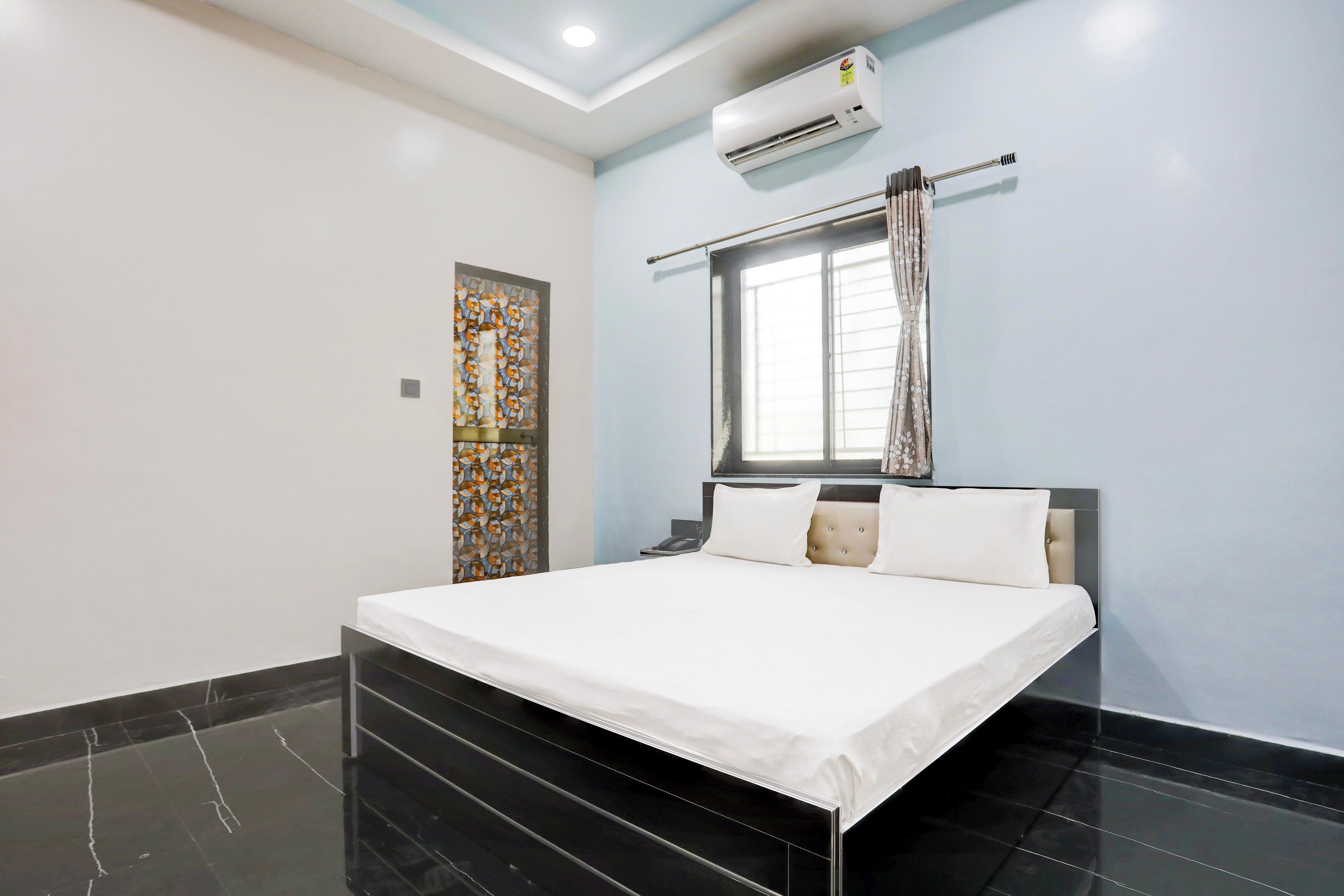 Une chambre d’hôtel comprenant un lit, une fenêtre avec des rideaux, un appareil de climatisation et un élément décoratif mural.