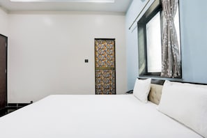 Ein Hotelzimmer mit einem Bett, einem Fenster mit Vorhängen, einer Tür mit einem Muster und einem Lichtschalter an der Wand.