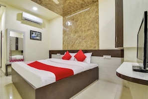 Habitación de hotel con cama, televisión, espejo y equipo de aire acondicionado.