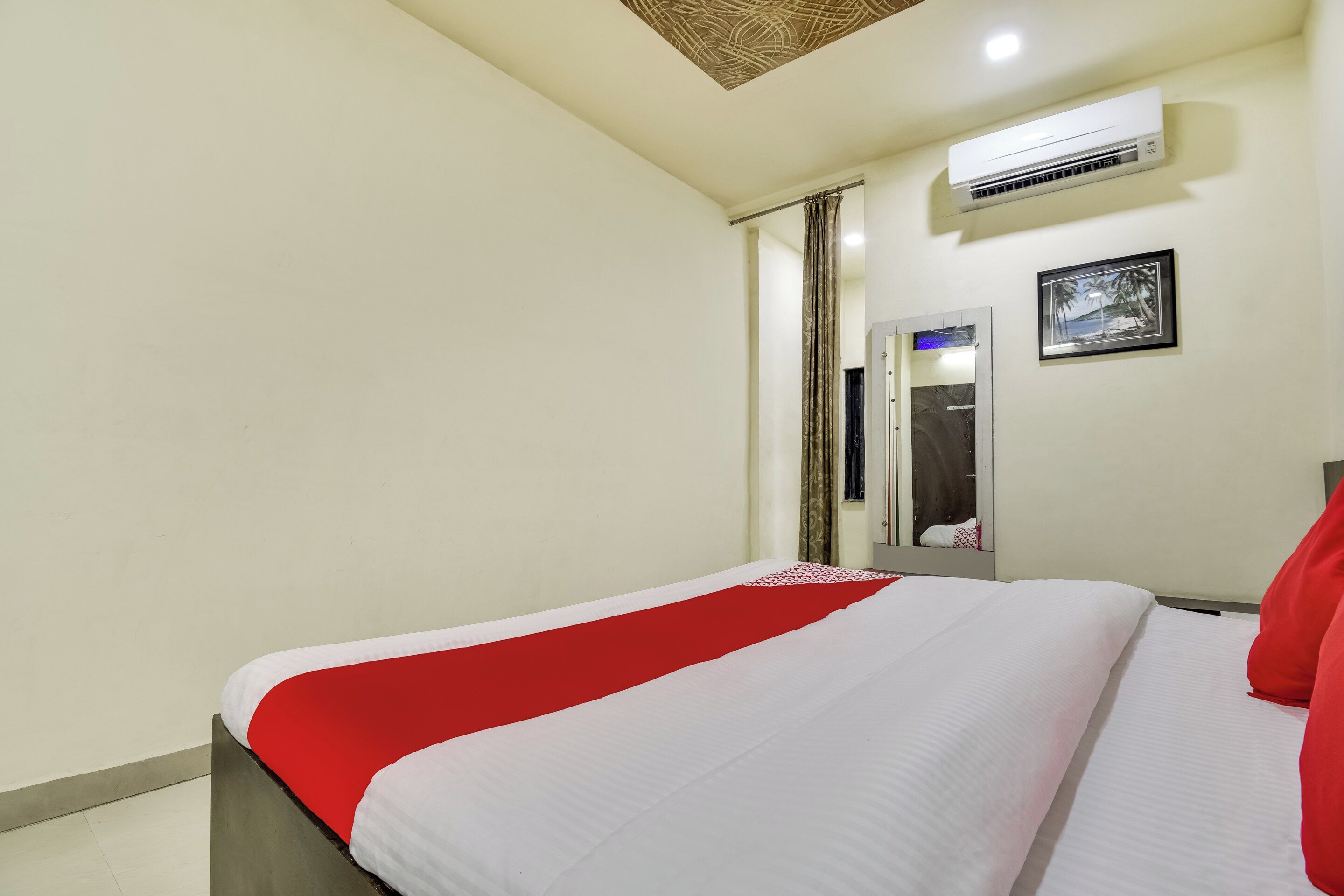 Una habitación de hotel con una cama, un espejo, un equipo de aire acondicionado y un cuadro en la pared.