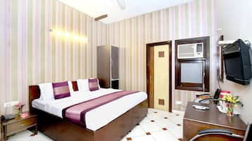 Una habitación de hotel con cama, mesita de noche, escritorio, silla, televisor y armario.