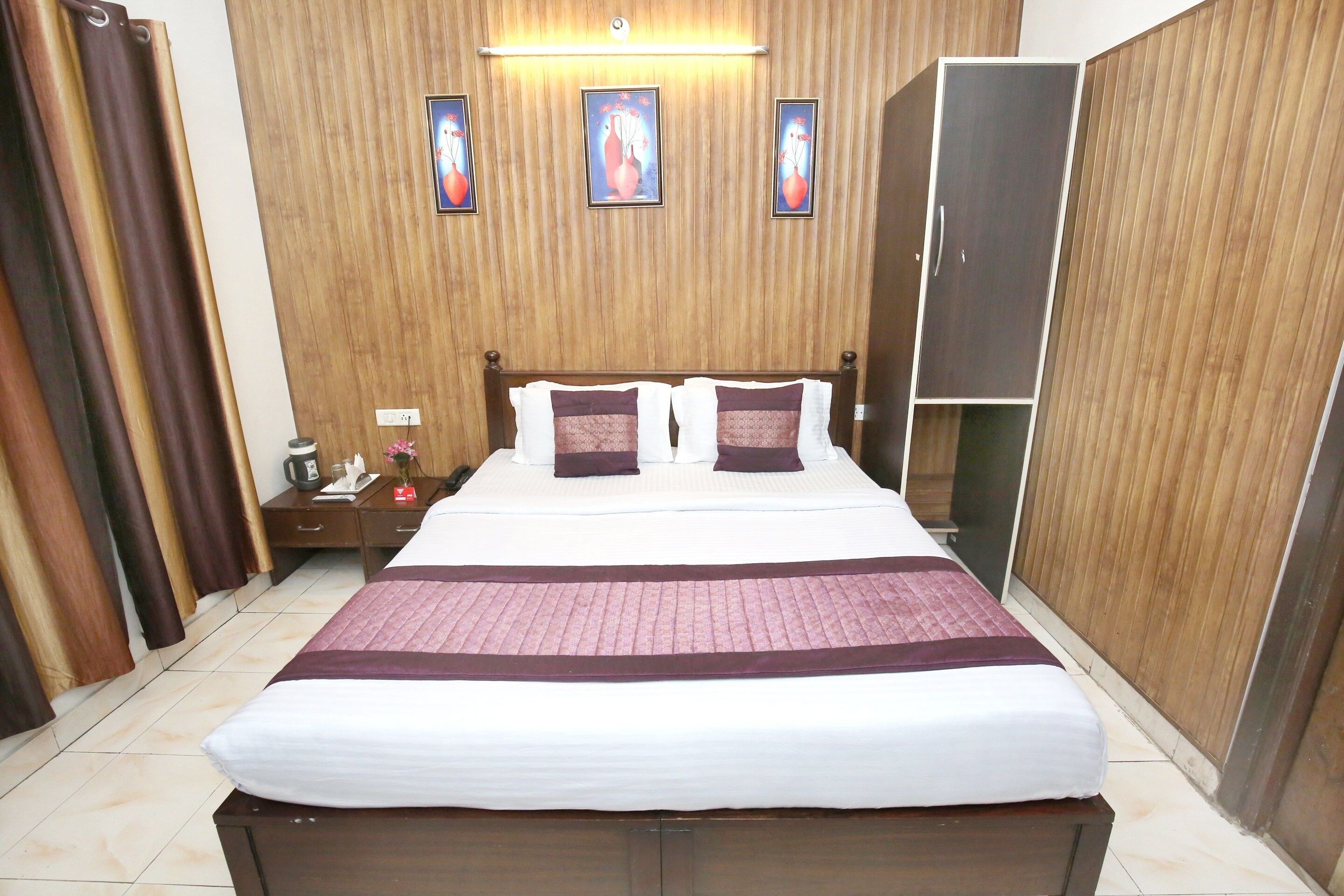 A hotel room with a bed, a nightstand, a wardrobe, and a wall with three framed pictures.