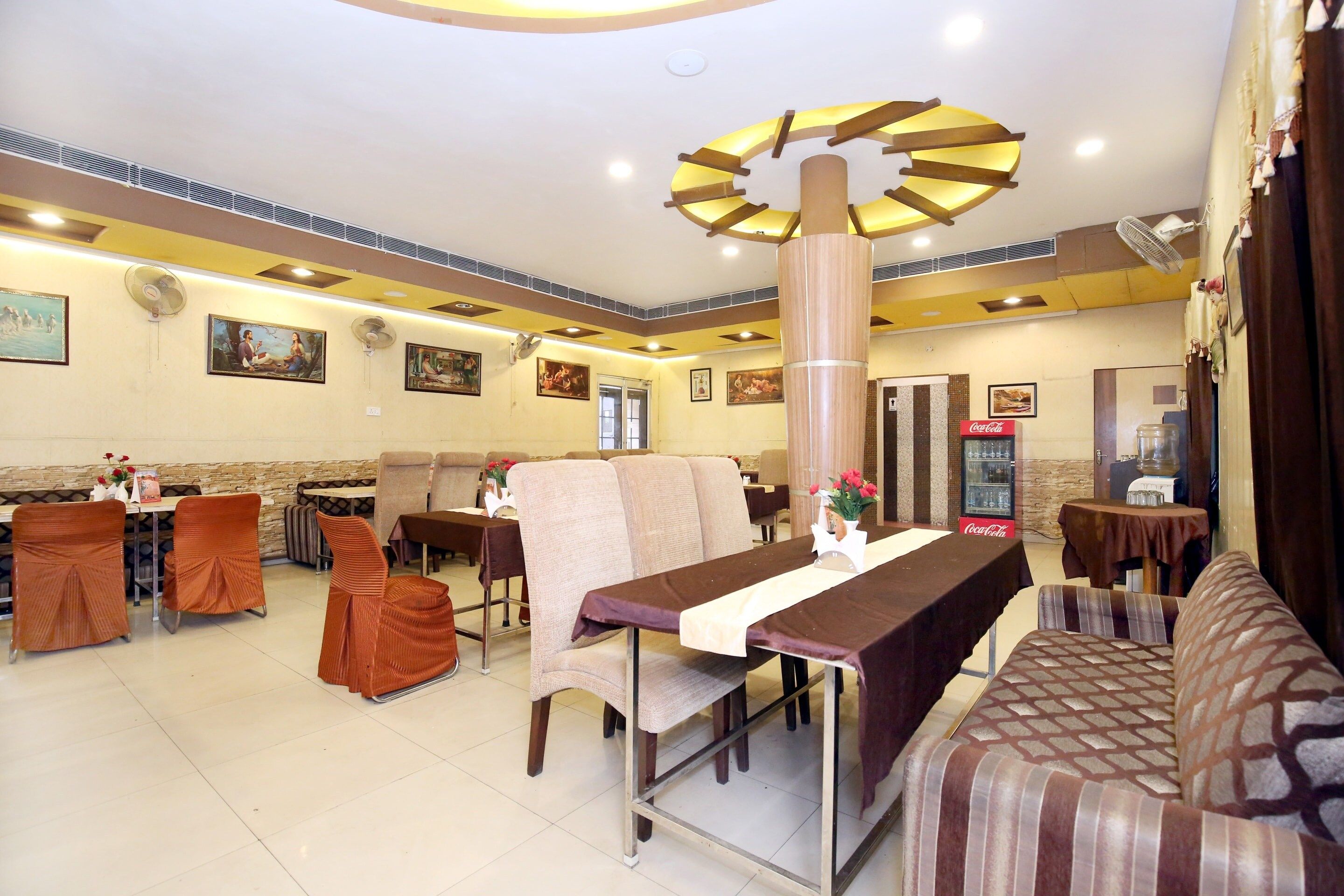 A restaurant with multiple tables and chairs, a large fan, and wall-mounted artwork.