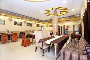 A restaurant with multiple tables and chairs, a large fan, and wall-mounted artwork. - Hotel O H.K.Continental (Amritsar)