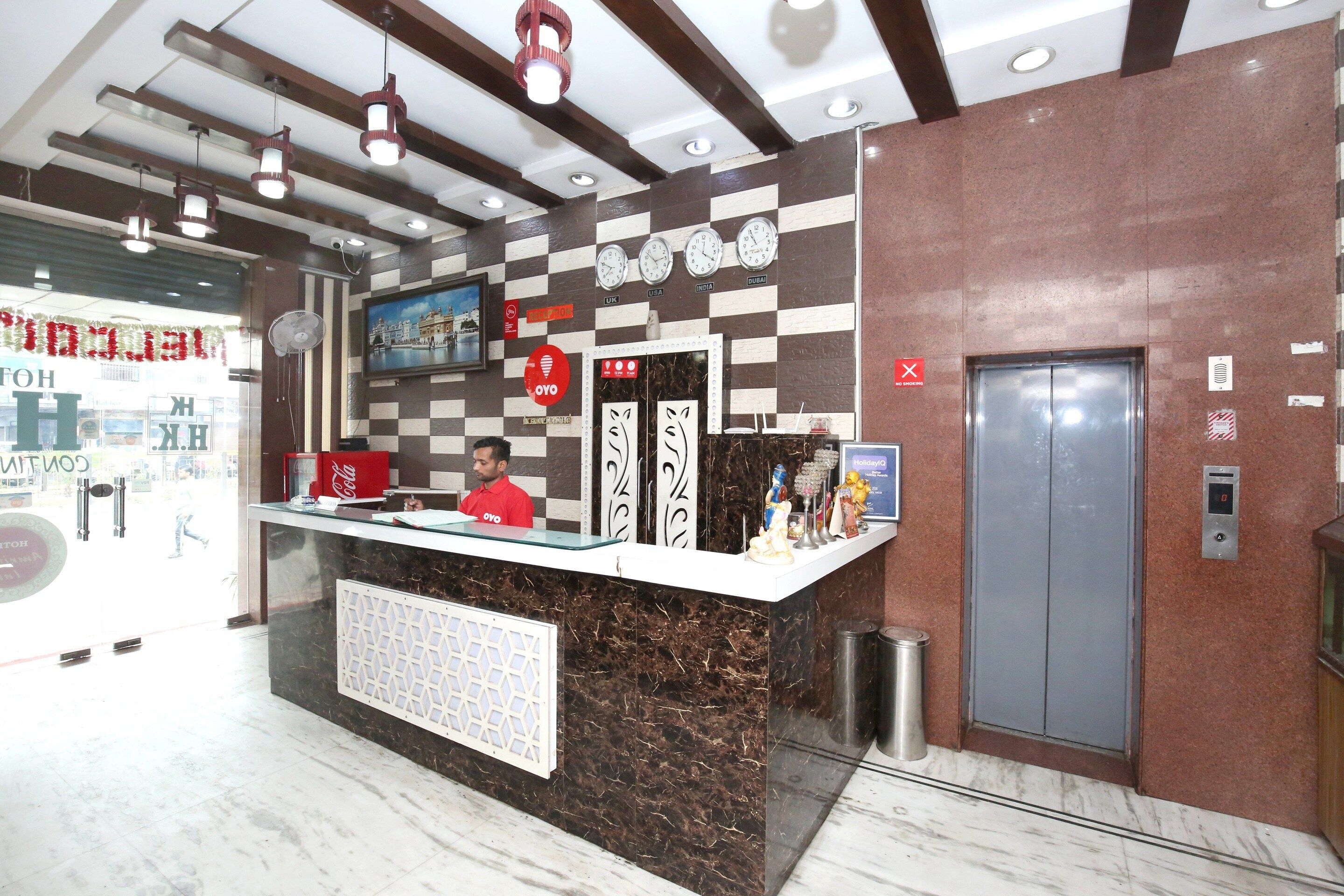 A hotel reception desk with a check-in counter, a Coca-Cola refrigerator, a digital clock, and a no-smoking sign.