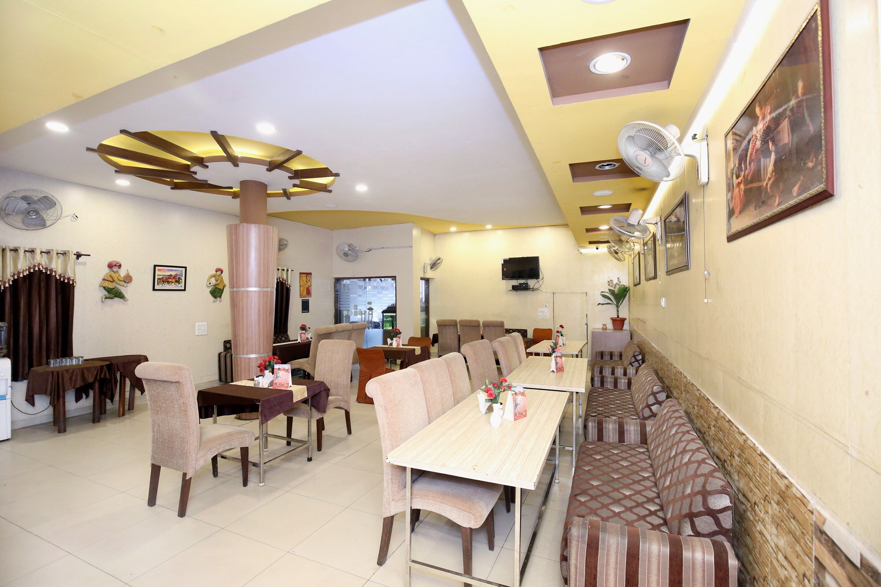 A dining area with multiple tables and chairs, a large pillar, ceiling fans, and a television mounted on the wall.
