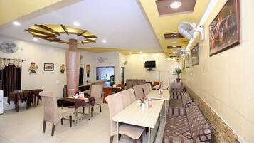 A dining area with multiple tables and chairs, a large pillar, ceiling fans, and a television mounted on the wall.