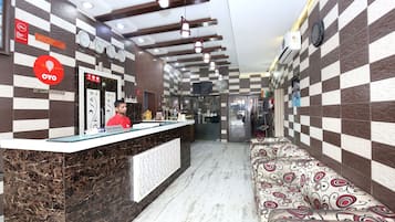 Zona de recepción de un hotel con mostrador, área de espera con tapicería estampada y una pared con relojes que marcan diferentes husos horarios.