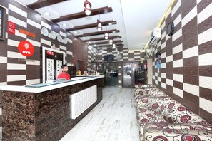 A hotel reception area with a reception desk, a seating area with patterned upholstery, and a wall with clocks indicating different time zones. - Hotel O H.K.Continental (Amritsar)