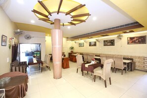 Un restaurante con varias mesas y sillas, un pilar central y ventiladores fijados a la pared.