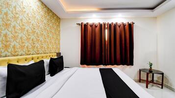 Quarto de hotel com cama, cabeceira, janela com cortinas, mesa de cabeceira e papel de parede estampado.