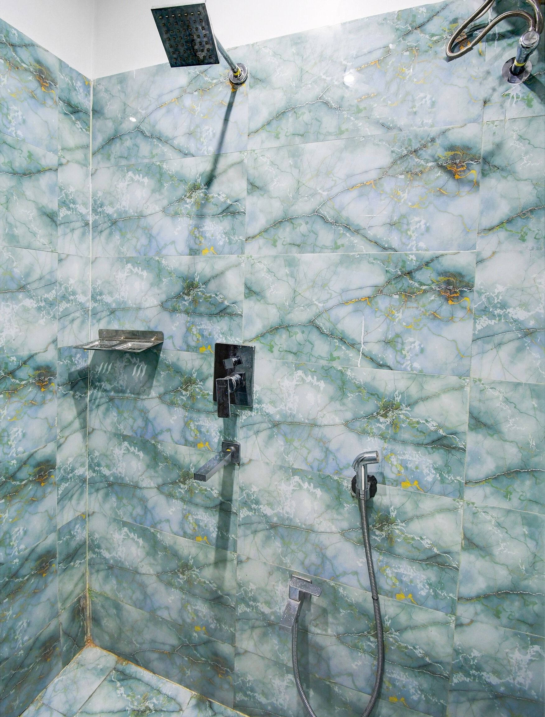 Un baño con zona de ducha que cuenta con una pared de mármol, un cabezal de ducha manual, un accesorio de ducha manual y un grifo empotrado.