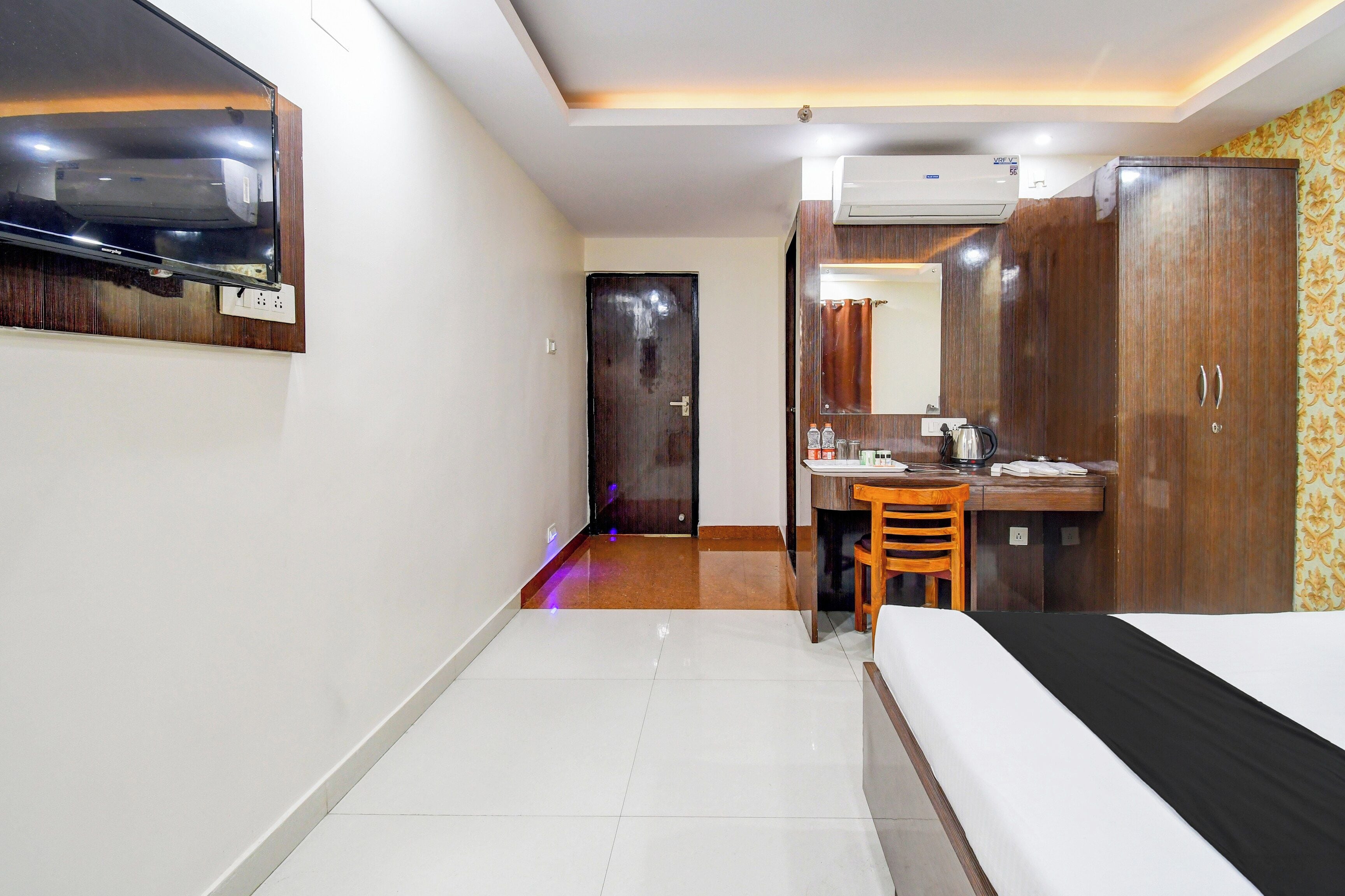 A hotel room with a bed, a desk, a chair, a wardrobe, and a mirror.