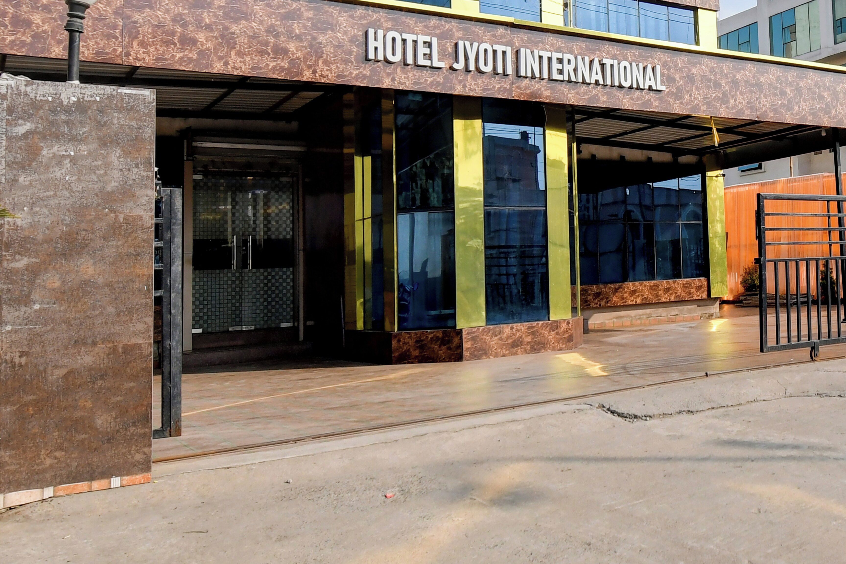 Exterior do Hotel Jyoti International com design moderno, destacando uma entrada imponente e uma área coberta com portas de vidro.