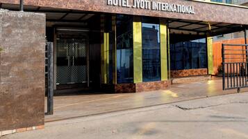 Exterior do Hotel Jyoti International com design moderno, destacando uma entrada imponente e uma área coberta com portas de vidro.