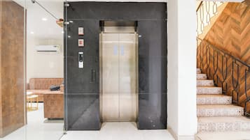 Um elevador com painel de comando, uma mesa de recepção e uma escada com guarda-corpo trabalhado.