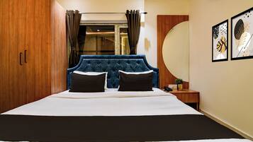 A bedroom with a large bed, a wooden wardrobe, a nightstand with a phone, and a wall with framed artwork.