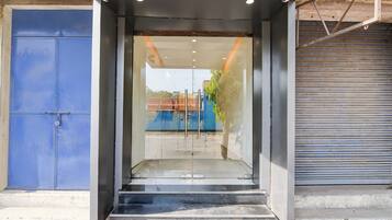 A modern entrance with a glass door, a blue door to the left, and a closed roller shutter to the right.