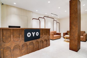 Un'area reception con una scrivania reception con la scritta 'OYO', una zona salotto con due divani e un tavolino, e un arredamento moderno.