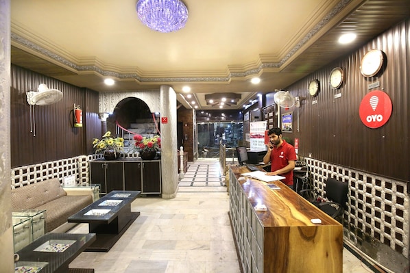 A reception area with a wooden reception desk, a seating area with a sofa and a table, and a decorative wall with clocks and a sign. - Hotel O Sallow International (Amritsar)