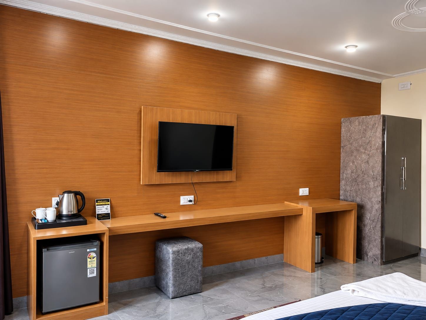 Habitación de hotel con pared de madera, un televisor de pantalla plana sobre un escritorio de madera, un minibar y un refrigerador.