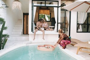 A poolside area with a seating arrangement, a small table with items, and a person tending to the table. - ASHITA by SEAOM Villas (Gianyar)