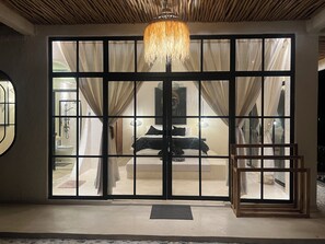 Ein Zimmer mit einer großen Schiebeglasdoor, die auf einen Balkon führt, einem Bett mit schwarz-weiß gestreifter Bettdecke und einer hängenden Leuchte.