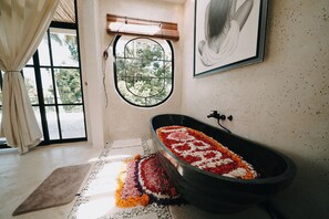 A bathroom with a freestanding bathtub filled with flower petals, a window with a view of greenery, and a towel rack. - ASHITA by SEAOM Villas (Gianyar)