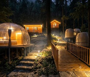 A series of dome-shaped accommodations connected by a wooden walkway, surrounded by a forested area. - the log hut dharamkot (Dharamshala)