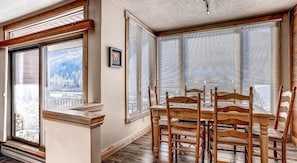 Zona pranzo con tavolo e sedie in legno, ampie finestre con persiane e vista su un paesaggio innevato.