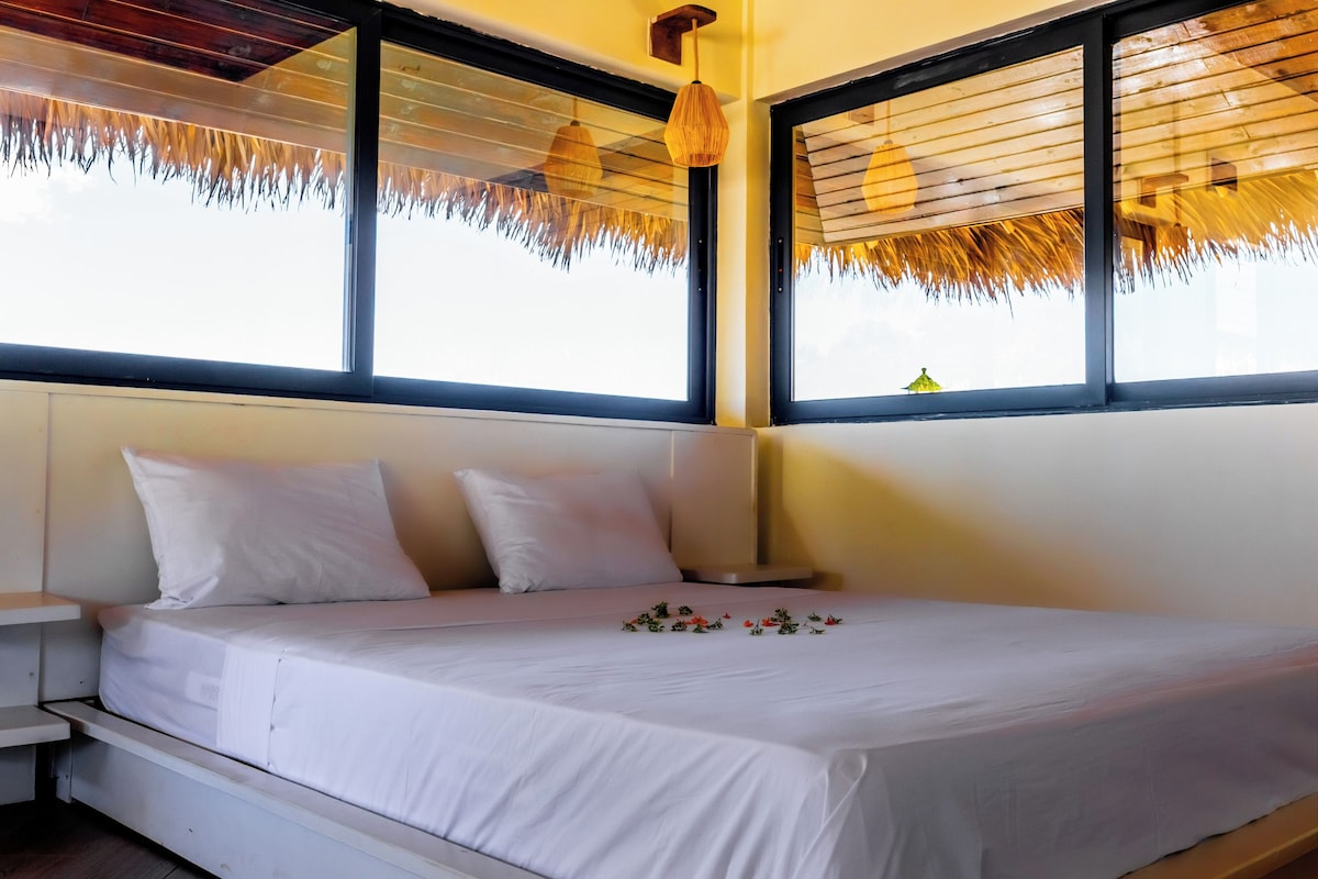 Una cama con ropa blanca, una mesita de noche y una ventana con persiana de madera.