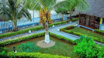 Un resort tropical con una palmera, una estructura de techo de paja y una cerca blanca.