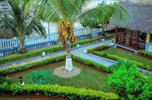 Un resort tropical con una palmera, una estructura de techo de paja y una cerca blanca.