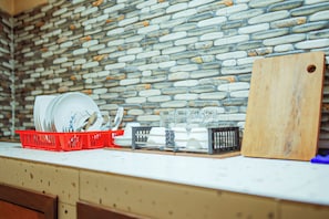 Una cocina con protector de piedra, un escurreplatos rojo, un portalápices negro y una tabla de cortar de madera.