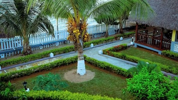 Un resort tropical con una palmera, una estructura de techo de paja y una cerca blanca.