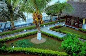 Un resort tropical con una palmera, una estructura de techo de paja y una cerca blanca.