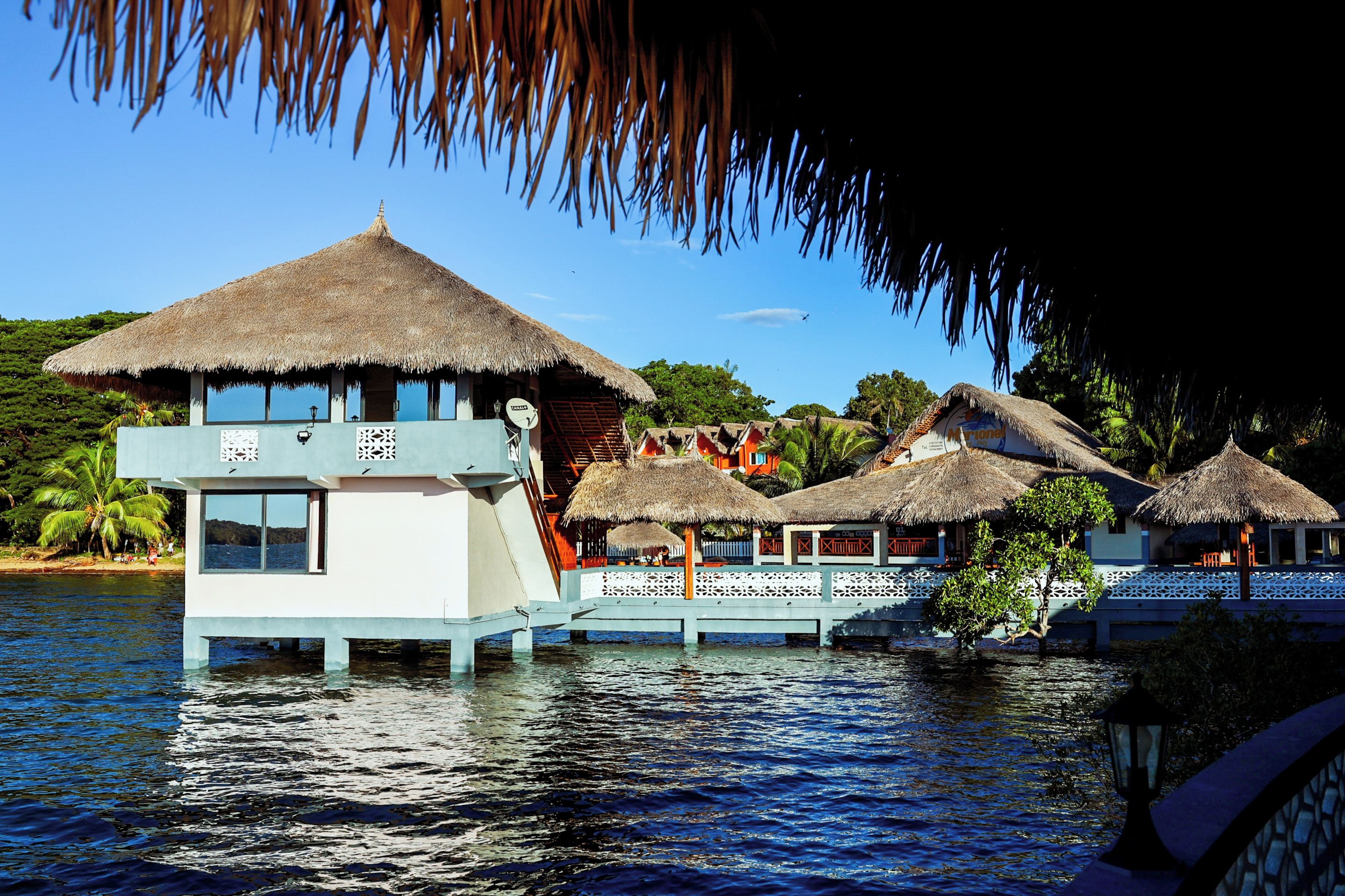 Des bungalows sur pilotis avec toits de chaume, offrant une vue sur l’eau et un ciel dégagé.