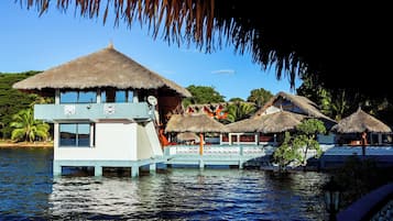 Bungalows sobre el agua con techos de paja, vista al agua y cielo despejado.