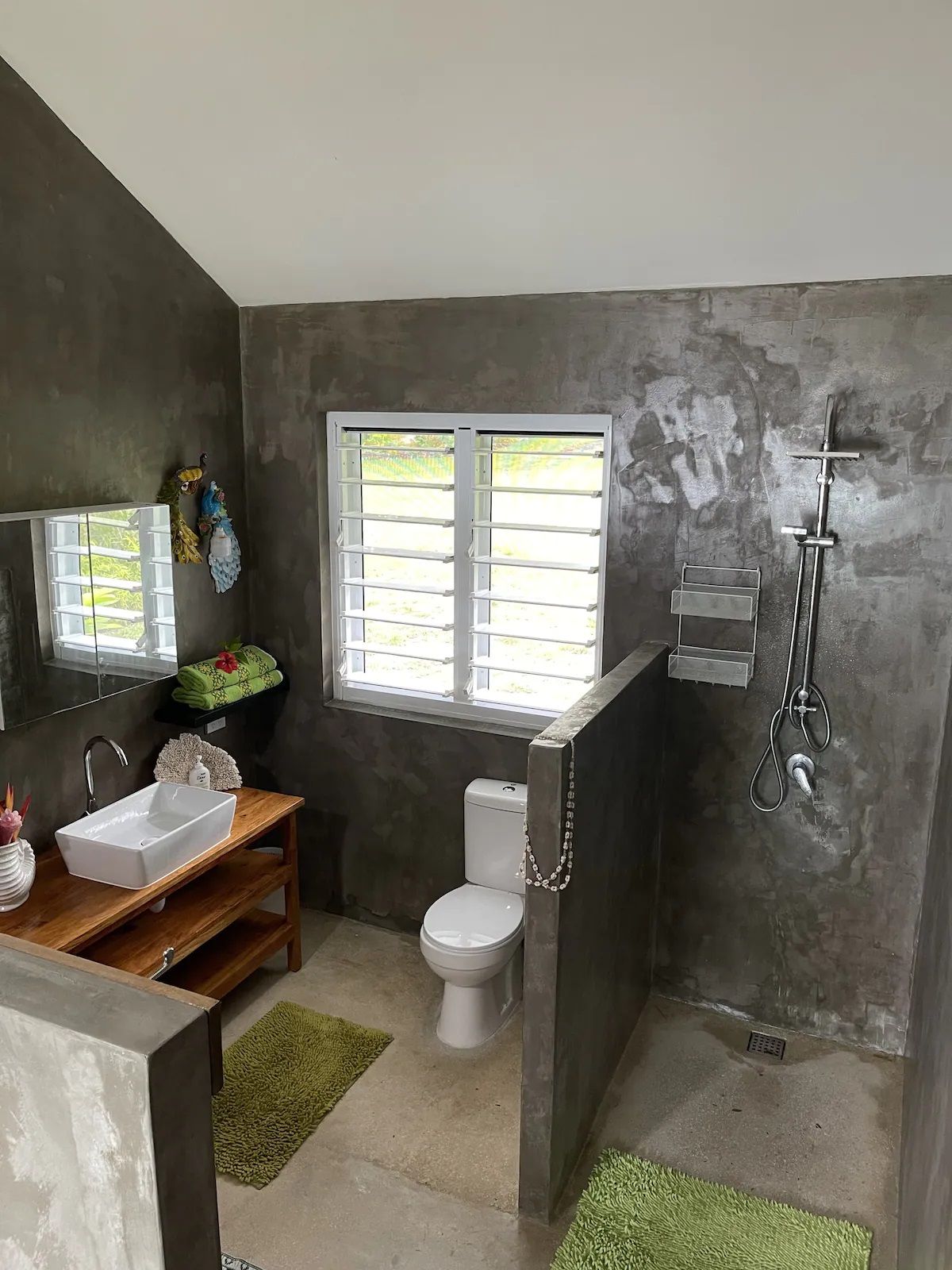 A bathroom with a white sink, a toilet, a shower, and a window with blinds.